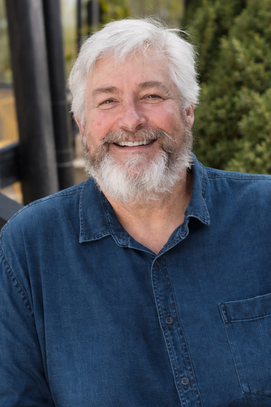 Man with white hair and beard wearing a blue shirt outdoors