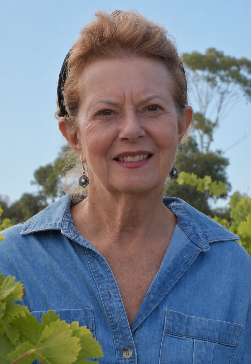 Woman wearing a blue denim shirt outdoors with greenery in the background